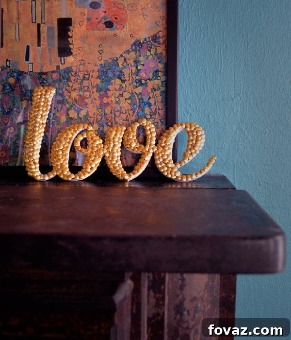 Applying the 'LOVE' word template to the foam core board using spray adhesive for a DIY letter art project.