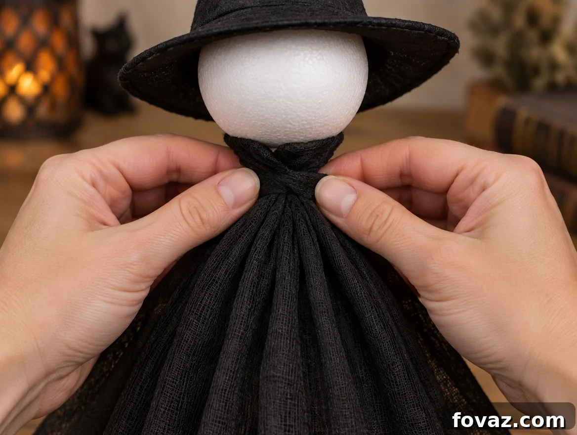 DIY Glowing Tomato Cage Witch: 4-Step Halloween Decor 5 Hands gathering and cinching black cheesecloth at the neck of a tomato cage witch to form shoulders